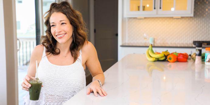 Alpha Queen Collective Blog - Queen Karissa Adkins - Spring Clean Your Body Why Detoxing is Essential for Women's Health - Karissa sitting at counter with vegetables and holding a green smoothie